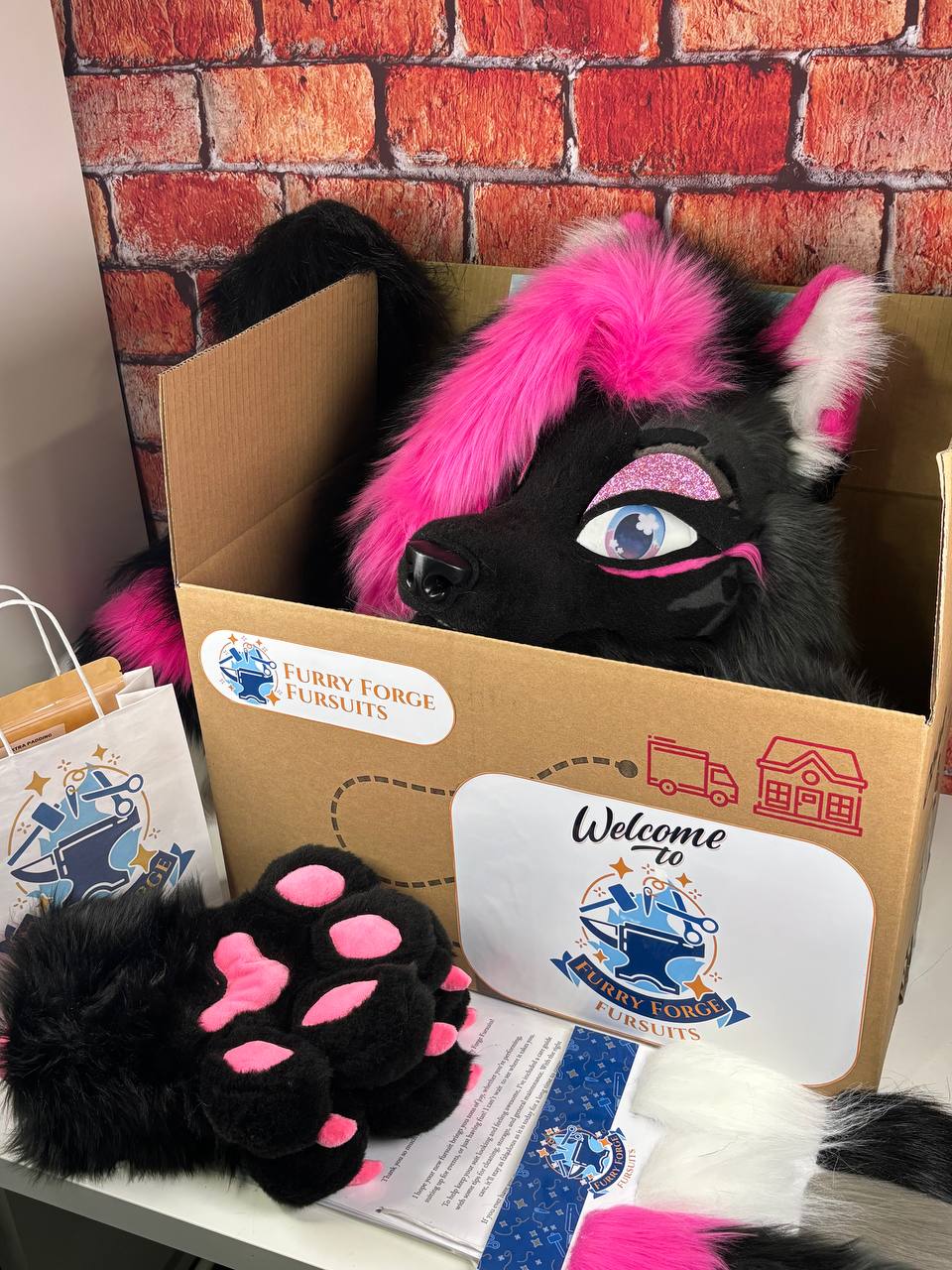 Furry forge fursuit with pink accents in a box against a brick wall background