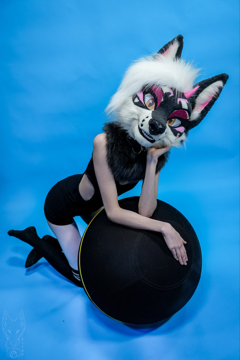 Person wearing a fox mask sitting on a black hat against a blue background